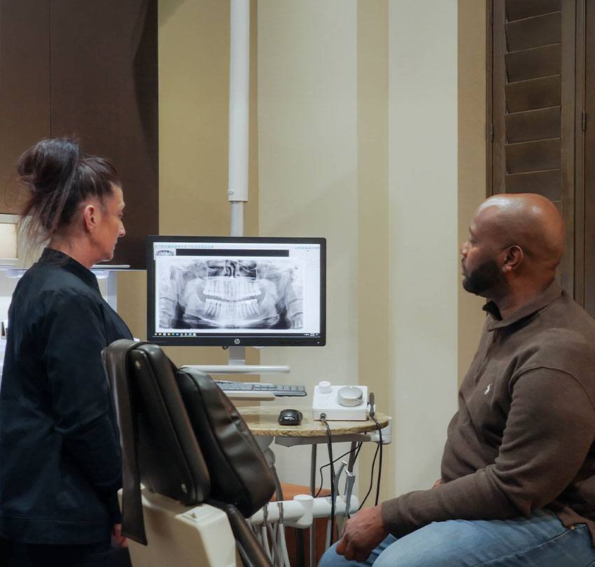 A female dental staff member and a male patient looks at an image in a monitor